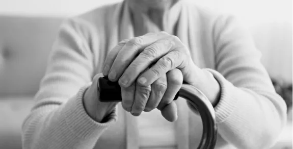 An older woman's hands on the top of a cane